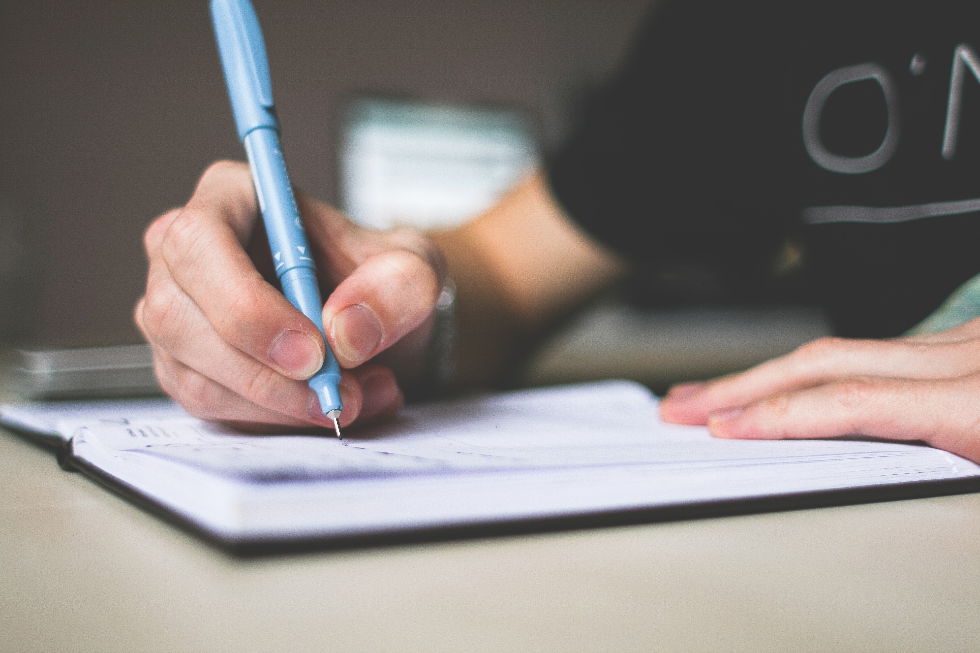 person-holding-blue-ballpoint-pen-writing-in-notebook-210661